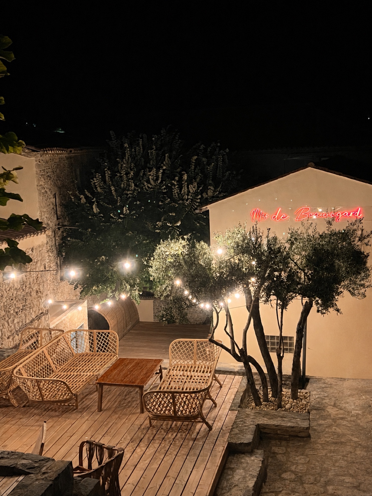 Terrasse du Mas Beauregard la nuit, enseigne néon et oliviers